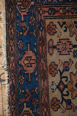 Vintage Hamadan rug close-up: indigo geometric border, dark beige field motifs, tattered fringe.