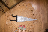 Vintage style gray felt Bedford pennant with white letters and black trim.