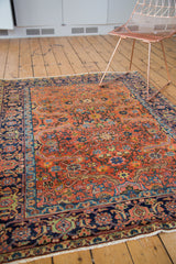 Vintage Heriz rug corner featuring peach field, curvilinear leaf motifs, navy border, white fringe.