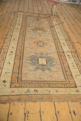 Antique Caucasian runner end, revealing geometric border motifs and tattered fringe in pale gold, charcoal, blush.