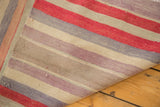 Folded Kilim rug corner, showing striped flatweave texture in faded red, mauve, ivory.