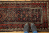 Feet standing on an antique Belouch rug, showcasing geometric pattern and time-softened tones.