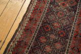 Antique Belouch rug showing visible wear, dark goat hair selvage, and wave motif border.