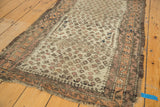 Corner of antique Belouch rug: pale terra cotta border, visible knot heads, tattered ends.