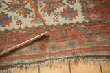 Tattered ends of vintage Belouch rug, showing geometric madder root red and sky blue motifs.