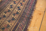 Geometric starbursts, navy, aubergine, and camel tones on an antique Belouch rug's tattered edge.