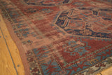 Geometric brick red and blue floral motifs on a vintage Caucasian carpet, showing varied pile.