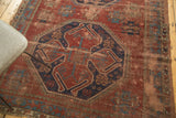 Vintage Caucasian carpet's navy geometric medallion, brick red field, and noticeable wear.