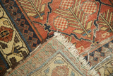 Folded corner of antique Hamadan rug, revealing cinnabar lily pattern, tattered fringe, and woven reverse.