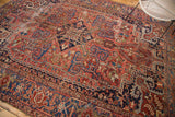 Vintage Heriz carpet with geometric vinery and budding flowers, featuring brick red, navy blue, and worn pile.