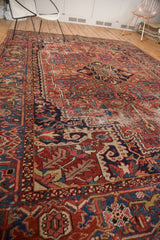 Heriz carpet's geometric vinery, brick red, navy, saffron, and gold hues with varied pile.