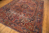 Vintage Heriz rug corner displaying geometric vinery, deep red field, navy border, and pile wear.