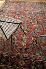 Distressed Heriz rug with brick red field and bold serrated patterns in blue and gold.