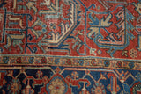 Close-up of distressed Heriz carpet with brick red, navy, and beige geometric floral designs and textured wear.