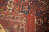 Unrestored tattered edge of an antique Afshar carpet, exposing red and indigo geometric motifs.
