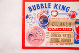 Close up of Mid Century Bubble King toy packaging artwork with blue text and a pink wand.