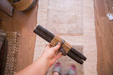 Pair of black beeswax taper candles, bundled and held by a hand, 12 inches tall.