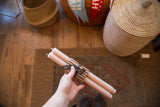 A pair of blush beeswax taper candles with a smooth finish, wrapped in corrugated paper.