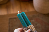Turquoise beeswax taper candles, wicks visible, in natural cardboard wrap.