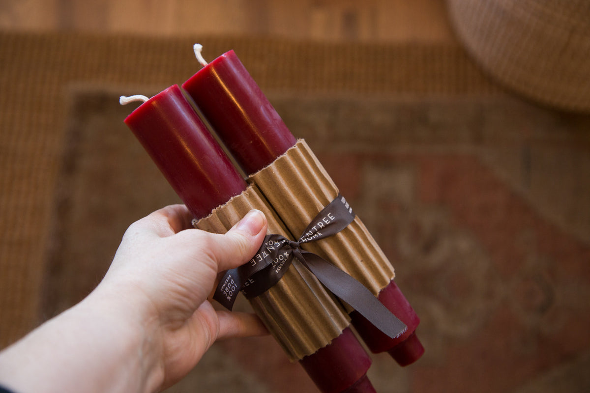 A pair of bittersweet red beeswax column taper candles with corrugated wrap and ribbon.