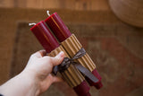 A pair of bittersweet red beeswax column taper candles with corrugated wrap and ribbon.