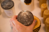 Distressed zinc lid of a vintage jelly jar candle, showing embossed 