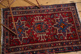 Persian Karaja rug corner with fringe, showcasing cherry red, navy, and teal geometric-curvilinear motifs.