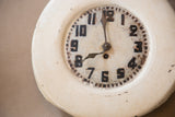 Distressed off-white clock face, showing hand-painted black numbers and aged hands.
