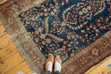 Deep indigo Farahan Sarouk rug with terra cotta border, floral vines, serrated leaves, person's feet.