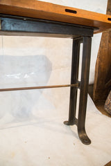 Dark iron leg and threaded copper-toned metal crossbar of the industrial work table.