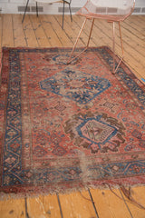Distressed lower corner of an antique Hamadan rug, showing tattered ends and muted floral patterns.