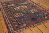 Worn pile and tattered fringe on the corner of this Antique Fachralo Kazak rug in brick red and teal.