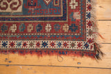 Antique Fachralo Kazak rug's frayed ends and geometric brick red, teal border.