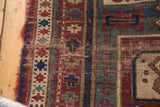 Antique Fachralo Kazak rug: tattered fringed end with geometric red, teal, and beige patterns.