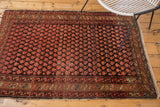 Vintage Hamadan rug's tattered edge, bronze border, and cranberry blush boteh field.