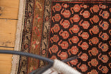 Vintage Hamadan rug detail: repeating cranberry blush boteh on chocolate brown, showing tattered side.