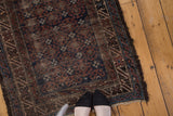 Distressed vintage Belouch rug showing allover crab motif, indigo, brown, ivory tones, tattered ends.