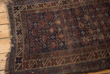 Distressed corner of a vintage Belouch rug with tattered fringe and indigo crab pattern.
