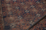Vintage Belouch rug's distressed texture, revealing indigo blue and earthy brown geometric motifs.