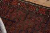 Repeating gul motif on vintage Afghan rug, brick red, charcoal, and navy hues, soft patina.