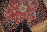 Distressed vintage Malayer rug featuring cinnabar red and charcoal Herati motifs under boots.