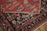 Distressed cinnabar red Malayer rug corner with intricate charcoal border design and fringe.
