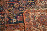 Antique Kamseh rug detail: indigo field, madder red border, geometric motifs, and hand-stitched edge.