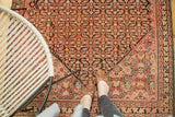 Antique Malayer rug's corner with repeating Herati motif in blush, indigo, and geometric forms.