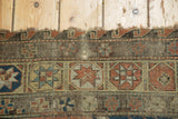 Detail of antique Soumac carpet showing tattered border, geometric star motifs, and charcoal tones.