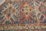 Vivid navy, red, and saffron geometric eagle motif with exposed foundation on antique Soumac rug.