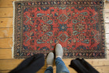 Persian Lilihan rug with cinnabar red field, powder blue florals, and worn fringed edge.