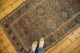 Angled corner of a vintage Kurdish rug, displaying geometric gul motifs and distressed earthy tones.