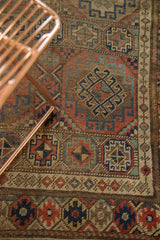 Geometric gul motif and distressed pile of vintage Kurdish rug in brown, red, and blue.