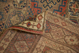 Kurdish rug corner folded, showing red, blue, brown gul motifs and hand-knotted reverse.
